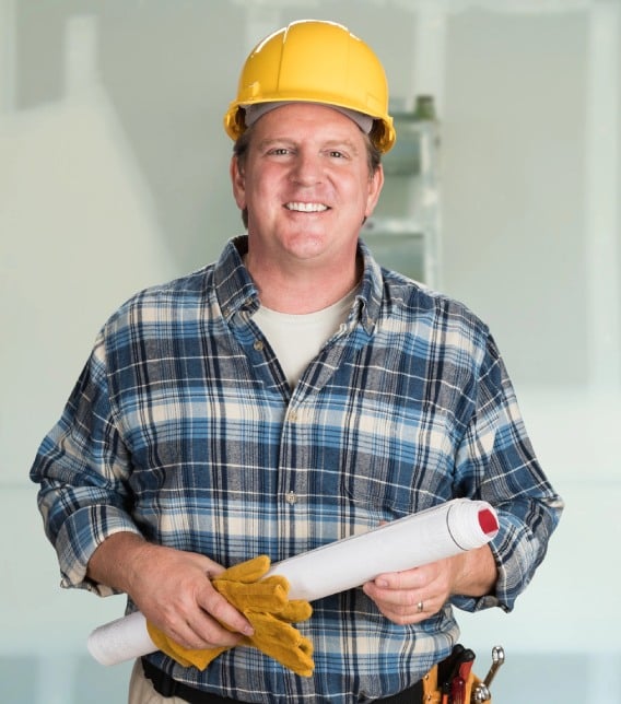 contractor with plans and hard hat in front of drywall